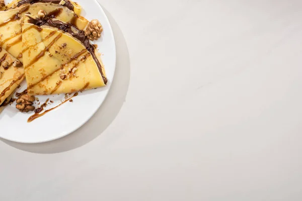 Vista dall'alto di gustose crepes con crema al cioccolato e noci su piatto su fondo grigio — Foto stock