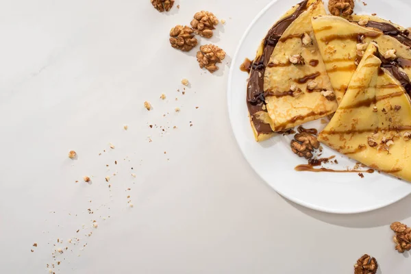 Top view of tasty crepes with chocolate spread and walnuts on plate on grey background — Stock Photo