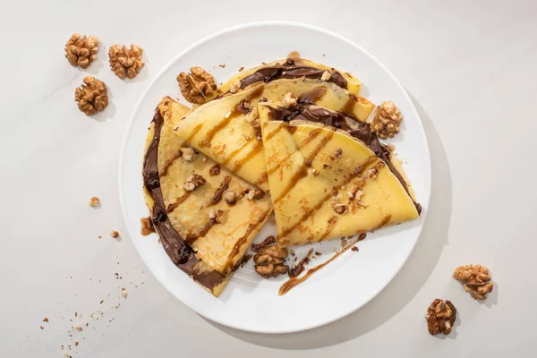 Вид сверху на вкусные блины с шоколадом и орехами на тарелке на сером фоне — стоковое фото
