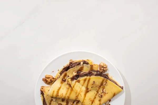 Top view of tasty crepes with chocolate spread and walnuts on plate on grey background — Stock Photo