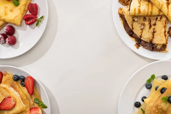 Vista dall'alto di gustose crepes con crema al cioccolato, noci e bacche su piatti su fondo grigio — Foto stock