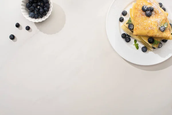 Vue de dessus des crêpes savoureuses près du bol de bleuets sur fond gris — Photo de stock