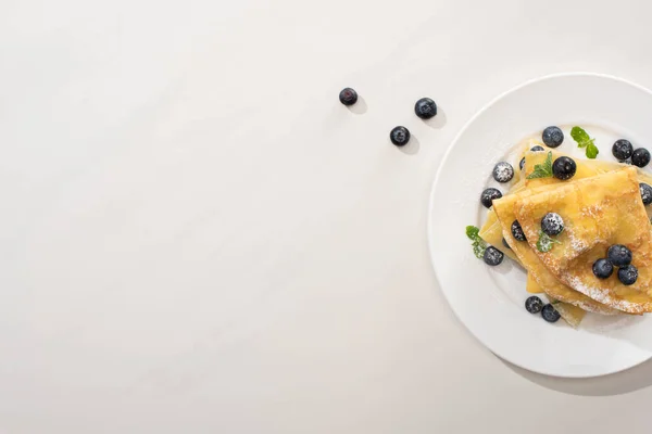 Draufsicht auf leckere Crêpes mit Blaubeeren und Minze auf Teller auf grauem Hintergrund — Stockfoto