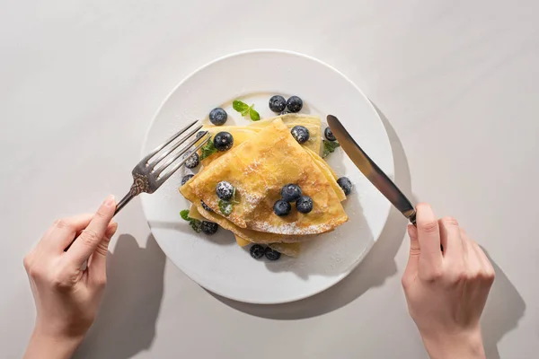 Vista ritagliata di donna mangiare crepes gustose con mirtilli e menta su sfondo grigio — Foto stock