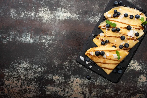 Vue de dessus de crêpes savoureuses aux bleuets, menthe et flocons de noix de coco servis à bord sur fond texturé — Photo de stock