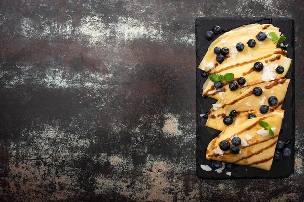 Vista superior de crepes sabrosos con arándanos, menta y copos de coco servidos a bordo sobre fondo texturizado - foto de stock