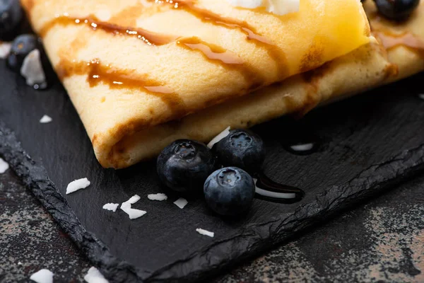 Close up view of tasty crepes with blueberries and coconut flakes served on board on textured background — Stock Photo