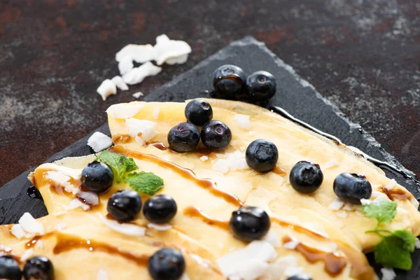 Vista de cerca de crepes sabrosos con arándanos, menta y copos de coco servidos a bordo sobre fondo texturizado — Stock Photo