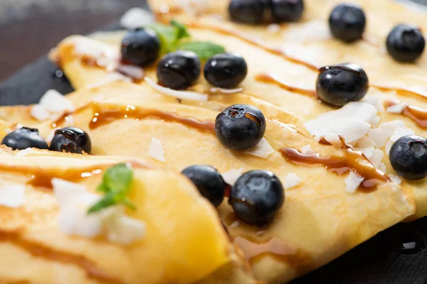 Vista da vicino di gustose crepes con mirtilli, menta e scaglie di cocco — Foto stock