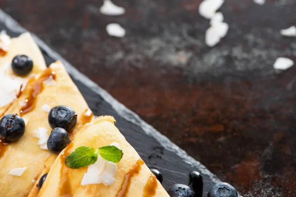 Vista de perto de crepes saborosos com mirtilos, hortelã e flocos de coco servidos a bordo em fundo texturizado — Fotografia de Stock