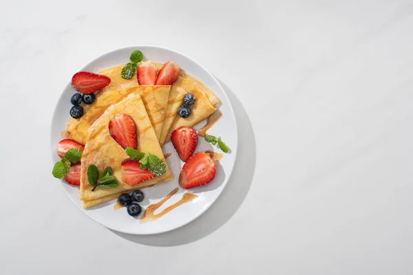 Vue de dessus de crêpes savoureuses aux bleuets, fraises et menthe sur assiette — Photo de stock