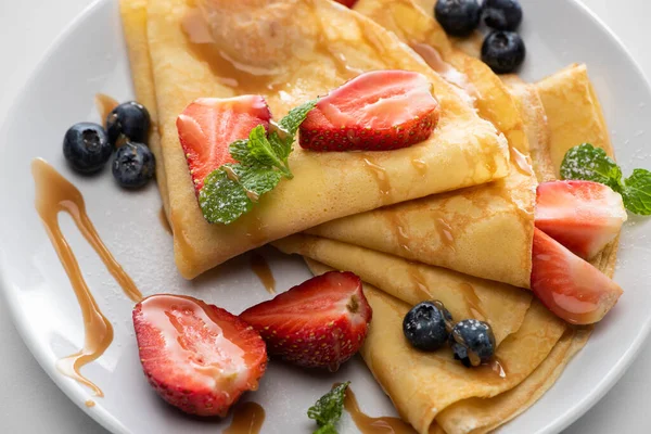 Vista de cerca de crepes sabrosos con arándanos, fresas y menta en el plato - foto de stock