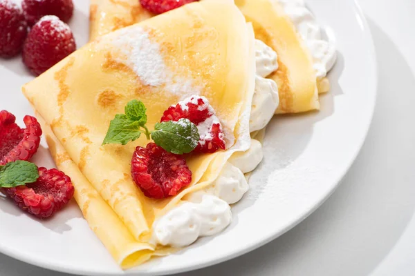 Primer plano vista de crepes sabrosos con frambuesas y crema batida en el plato - foto de stock