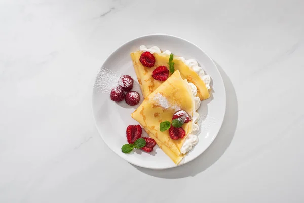 Top view of tasty crepes with raspberries and whipped cream on plate on grey background — Stock Photo