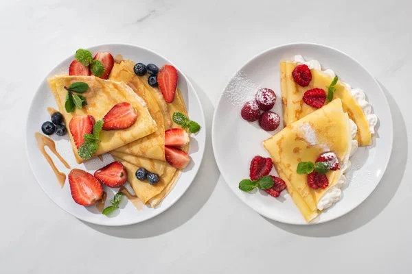 Draufsicht auf leckere Crêpes mit Beeren auf Tellern auf grauem Hintergrund — Stockfoto