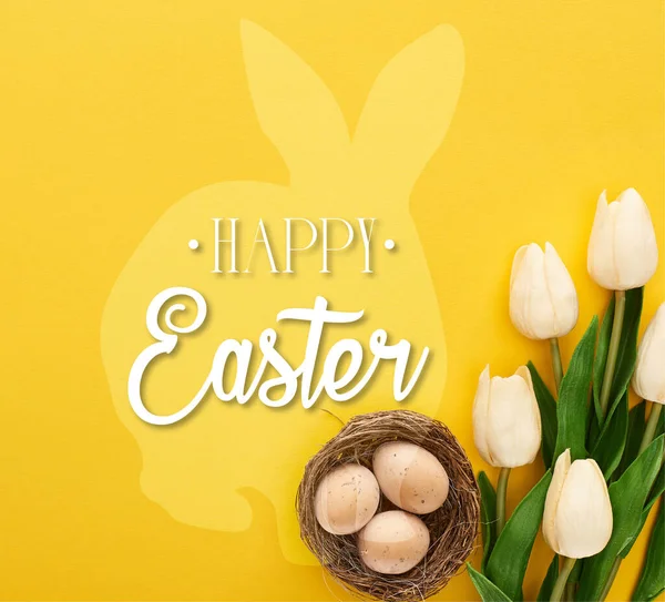 Top view of tulips and chicken eggs in nest on colorful yellow background with happy Easter illustration — Stock Photo