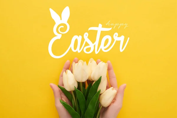 Vista recortada de la mujer sosteniendo tulipanes de primavera sobre fondo amarillo colorido con feliz ilustración de Pascua - foto de stock