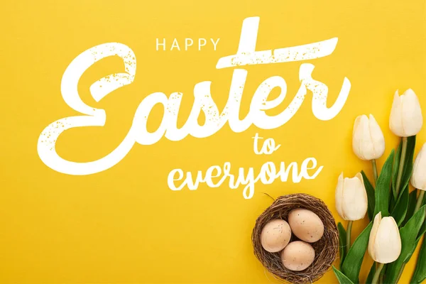 Top view of tulips and chicken eggs in nest on colorful yellow background with happy Easter to everyone illustration — Stock Photo