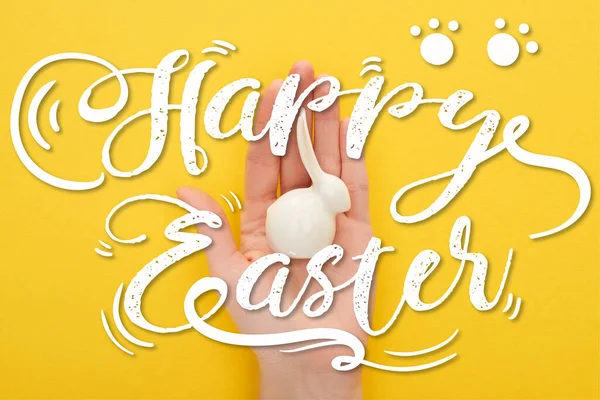 Cropped view of woman holding white Easter bunny on colorful yellow background with happy Easter illustration — Stock Photo