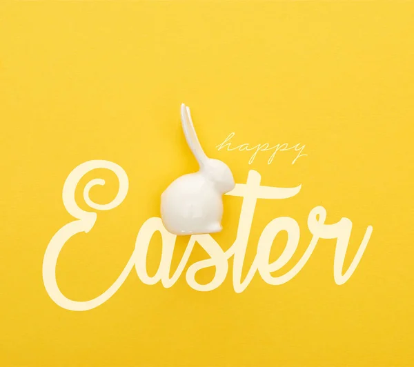 Vista superior de conejito de Pascua blanco sobre fondo amarillo colorido con feliz ilustración de Pascua - foto de stock