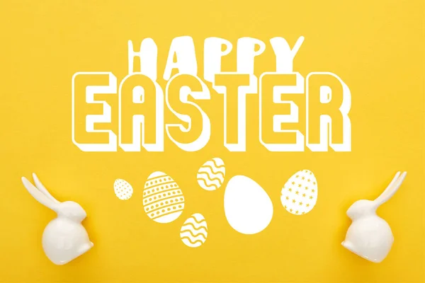 Vista superior de conejitos de Pascua blancos sobre fondo amarillo colorido con feliz ilustración de Pascua - foto de stock