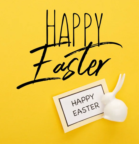 Top view of greeting card with happy Easter lettering near Easter white bunny on yellow colorful background — Stock Photo