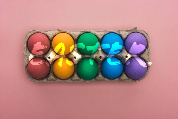 Вид зверху пофарбовані яйця в картонну коробку на рожевому фоні з великодніми ілюстраціями — стокове фото