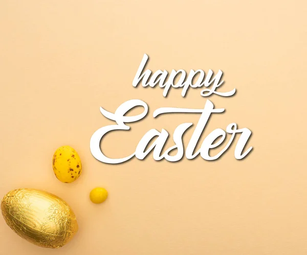 Top view of candy, quail and chocolate eggs on beige background with happy Easter illustration — Stock Photo