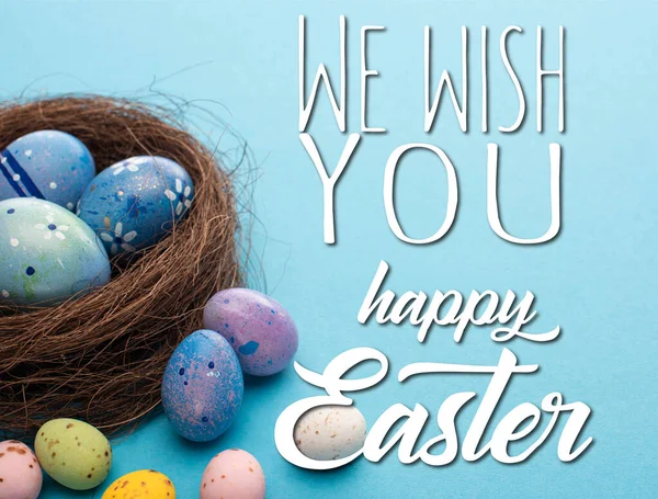 Nest and colorful chicken and quail eggs on blue background with we wish you happy Easter illustration — Stock Photo