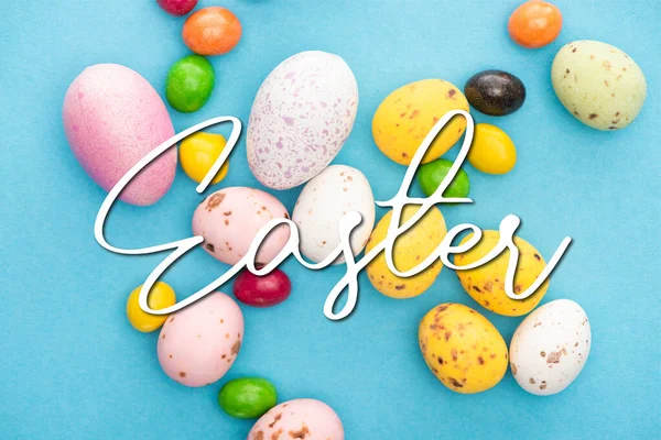 Top view of bright colorful sweets and easter eggs on blue background with Easter illustration — Stock Photo