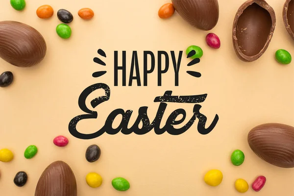 Top view of chocolate eggs and tasty sweets on beige background with happy Easter illustration — Stock Photo