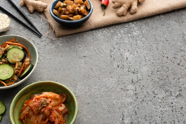 Selective focus of bowls with kimchi near chopsticks and ginger on concrete surface — Stock Photo