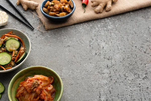 Enfoque selectivo de cuencos con kimchi cerca de palillos y jengibre en la superficie de hormigón - foto de stock