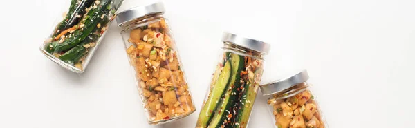 Panoramic shot of cucumber and daikon radish kimchi in jars on white background — Stock Photo