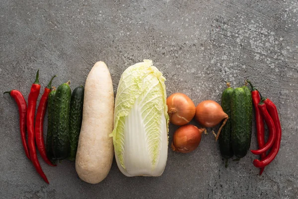 Top view of chili peppers, cucumbers, daikon radish, chinese cabbage and onions on grey concrete background — Stock Photo