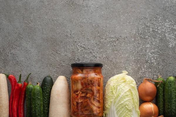 Vista superior de pimentas, pepinos, rabanete daikon, repolho chinês, cebolas e jarra de kimchi no fundo de concreto cinza — Fotografia de Stock