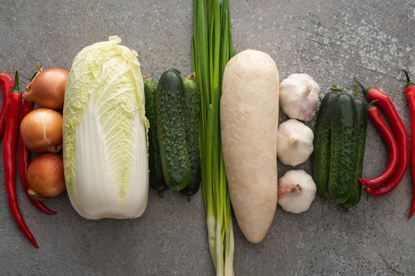 Vista superior de pimentas, cebolas verdes, pepinos, rabanete daikon, repolho chinês, cebolas e alho sobre fundo de concreto cinza — Fotografia de Stock