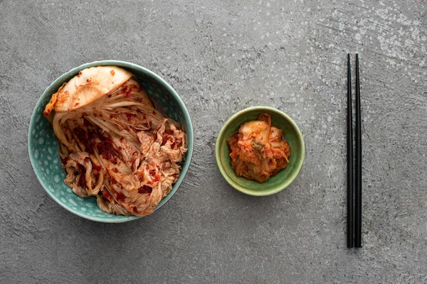 Vista superior de tigelas com kimchi saboroso e pauzinhos na superfície de concreto — Fotografia de Stock