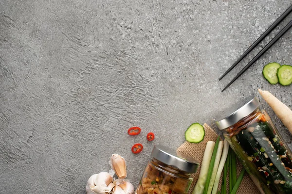 Vue de dessus de savoureux kimchi dans des bocaux, baguettes, oignons verts, gingembre et ail sur la surface du béton — Photo de stock