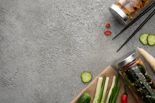 Blick von oben auf schmackhafte Kimchi in Gläsern, Essstäbchen, grünen Zwiebeln und Ingwer auf Betonoberfläche — Stockfoto