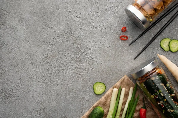 Vue de dessus de savoureux kimchi dans des bocaux, baguettes, oignons verts et gingembre sur la surface du béton — Photo de stock