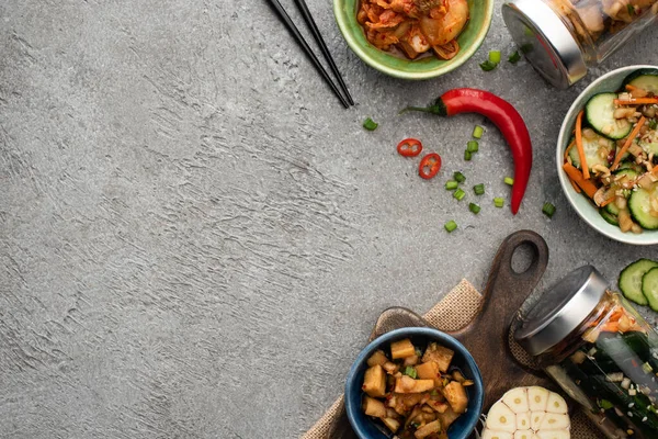 Vue de dessus des kimchi savoureux dans des bols et des bocaux, près des baguettes et du piment sur la surface du béton — Photo de stock