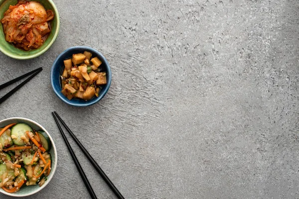 Vista superior de tigelas com kimchi saboroso perto de pauzinhos na superfície de concreto — Fotografia de Stock