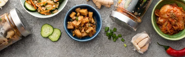 Plan panoramique de savoureux kimchi dans des bols et des bocaux près des baguettes, de l'ail et du piment sur la surface du béton — Photo de stock