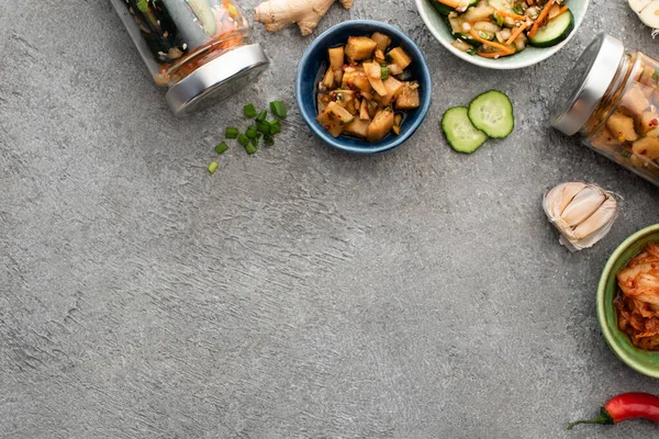 Top view of tasty kimchi in bowls and jars near ginger, garlic and chili pepper on concrete surface — Stock Photo