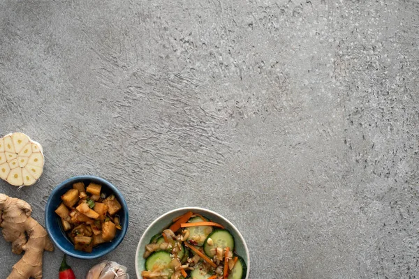 Vue de dessus de kimchi savoureux dans des bols près du gingembre et de l'ail tranché sur la surface du béton — Photo de stock