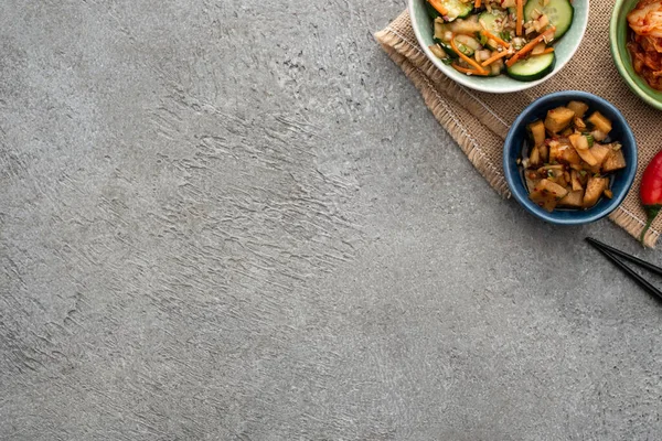 Vista superior de tigelas com kimchi saboroso ouvir pauzinhos na superfície de concreto — Fotografia de Stock