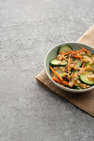 Bowl of delicious cucumber kimchi on sackcloth on concrete surface — Stock Photo