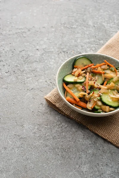 Tazón de delicioso kimchi de pepino sobre tela de saco en superficie de hormigón - foto de stock