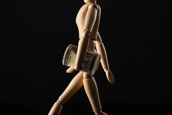 Wooden doll imitating walking with dollar banknotes isolated on black — Stock Photo